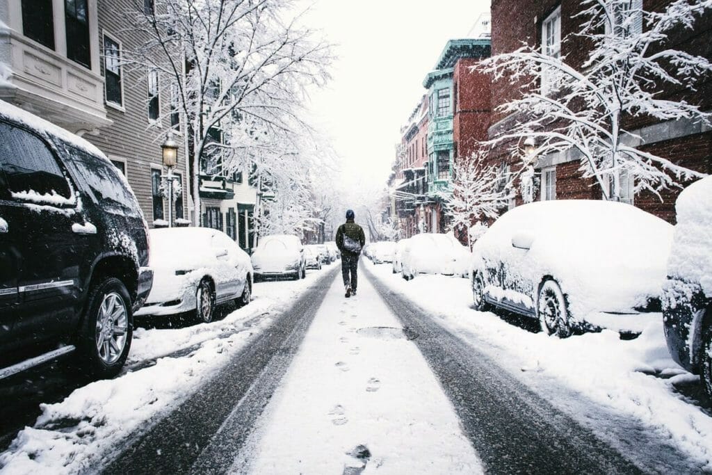 A man walking down the street with snow on the street 